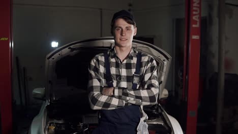 portrait of young handsome car mechanic in workshop, in the background of service. car repair, fault diagnosis, technical maintenance concept