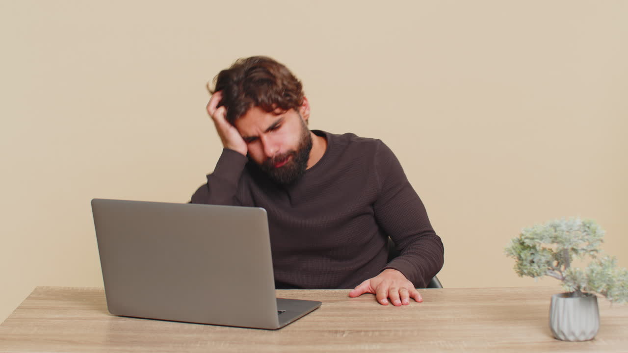 Young man using laptop at table loses becoming surprised sudden lottery results on beige background