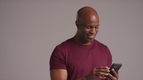 studio shot of smiling mature man with mobile phone getting good news against grey background 3