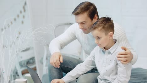padre con apendicitis abrazando a su hijo mirando la pantalla de la computadora en un apartamento moderno.