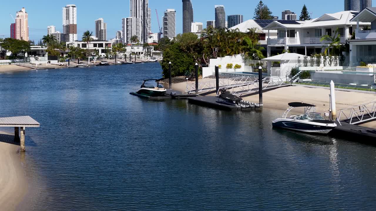 Motorboat approaches modern dock, luxury homes, city skyline, midday sunlight, smooth lateral camera movement