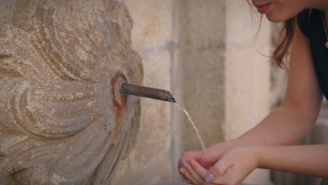 una chica se acerca a una fuente urbana y bebe agua en cámara lenta