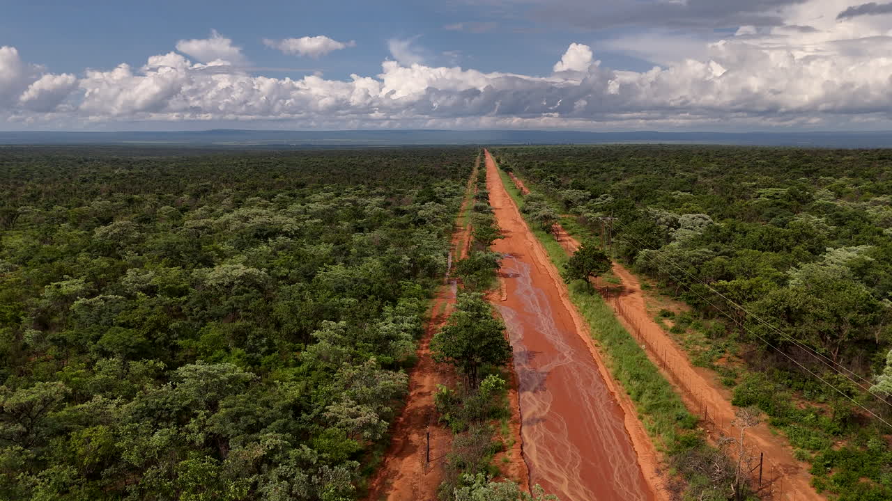 A long, red dirt road stretches through a lush African wilderness, serene and remote