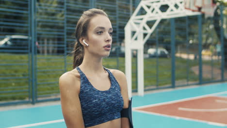 chica fitness con airpods haciendo sentadillas en la cancha deportiva en un día de verano