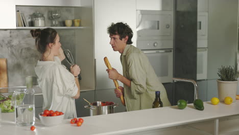 playful couple singing and dancing while cooking in the kitchen
