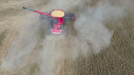 farm combine harvesting soybeans with trailed by a dust cloud on a midwestern farm, aerial drone