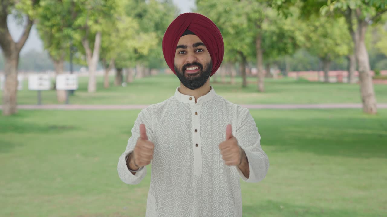 Uomo indiano Sikh felice che mostra il pollice in su al parco