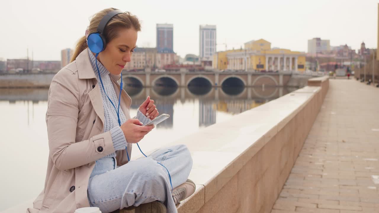 35 years old woman in headphones and listens to relaxing music and singing outdoor. Rest from office bustle and city noise