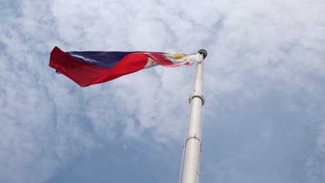 hermosa bandera nacional filipina volando a la izquierda con un gran viento mientras los pájaros vuelan por encima de ella y hermosas nubes esponjosas en el cielo