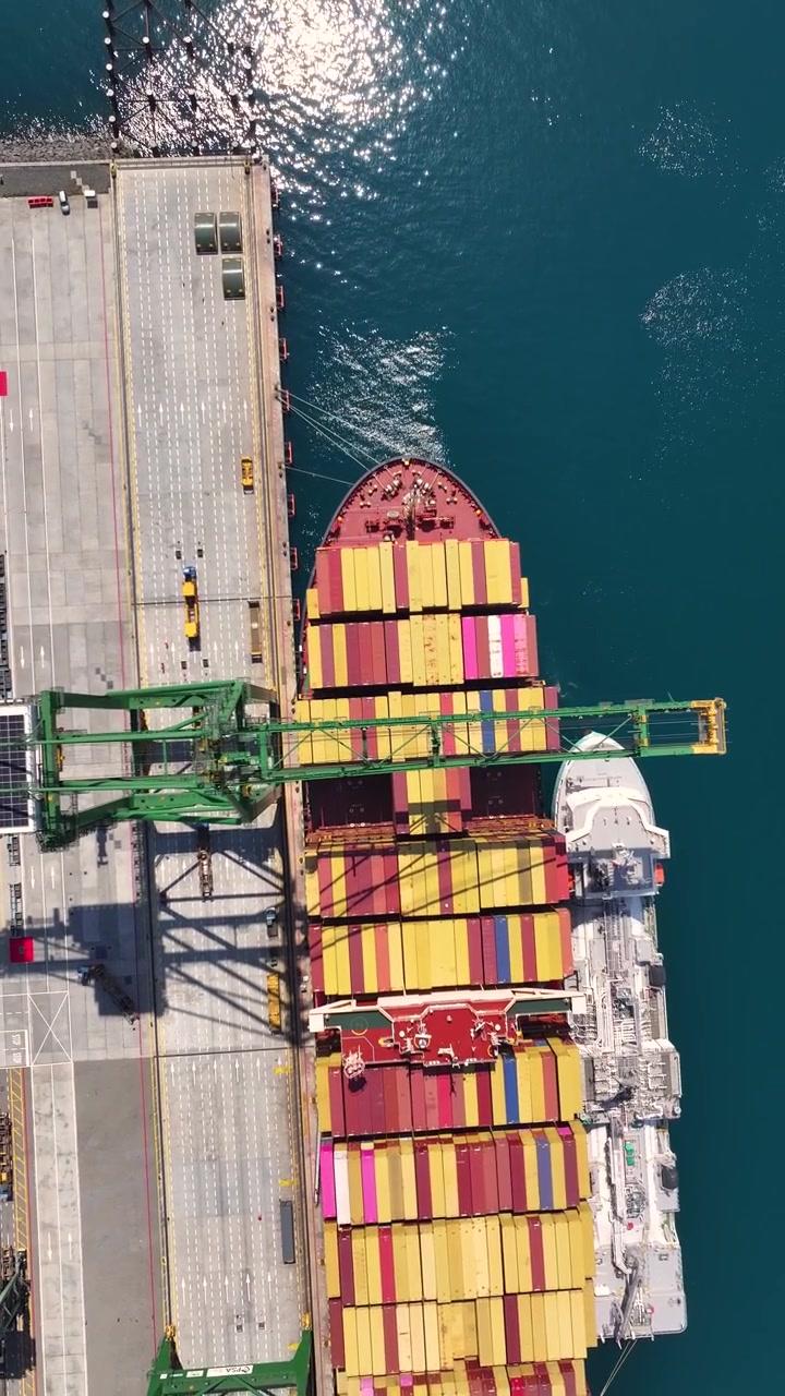 Container ship arrives at cargo terminal for unloading. Shipping containers are stacked on the dock. The terminal supports global shipping and international trade.