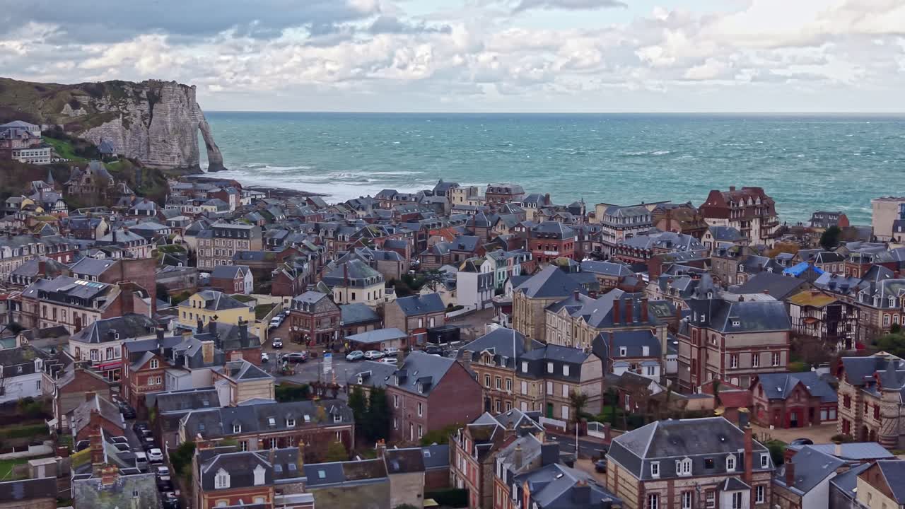 aerial drone view of the charming town of Etretat and the iconic Falaise d'Aval cliffs. The waves crash on the beach under a cloudy sky. Ideal for French travel and nature concepts, France