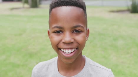 video portrait of smiling african american schoolboy in school playing field, with copy space