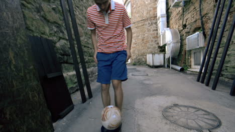 a young man kicks a soccer ball as he walks down an alleyway