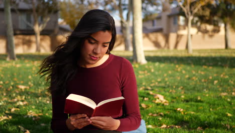 una joven colegiala estudiando y leyendo un libro en un césped del campus o en un parque al aire libre a cámara lenta