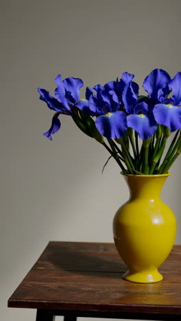 vibrant blue irises in a yellow vase on a wooden table