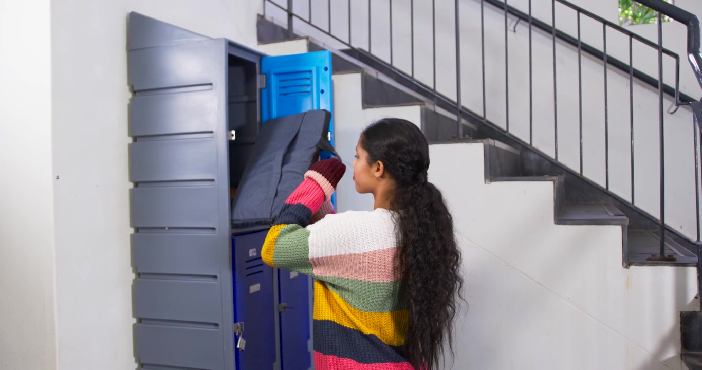 Gadis membutuhkan tas di loker dekat tangga, menggunakan perangkat genggam, membuka loker biru teratas, mengeluarkan tas