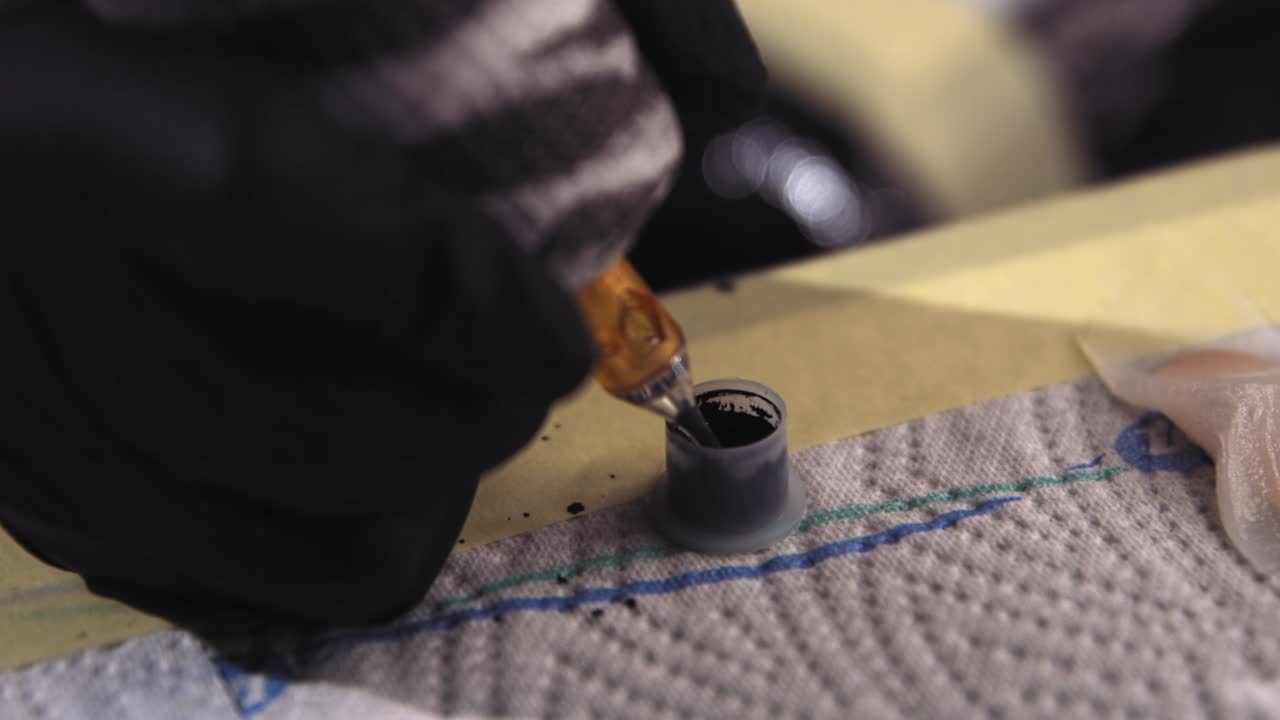 Slow motion footage of a tattoo gun's needle being dipped into a small container of black ink