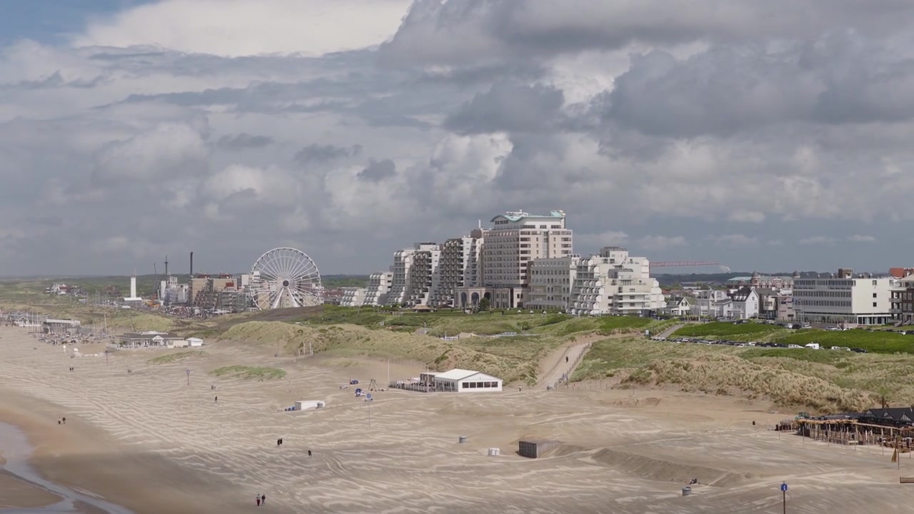 Noordwijk strand strækker sig under klitter og et pariserhjul, med hoteller og lejlighedstårne langs kystresortet nær Palaceplein, Sydholland, Holland, i en kredsende etablerende optagelse.