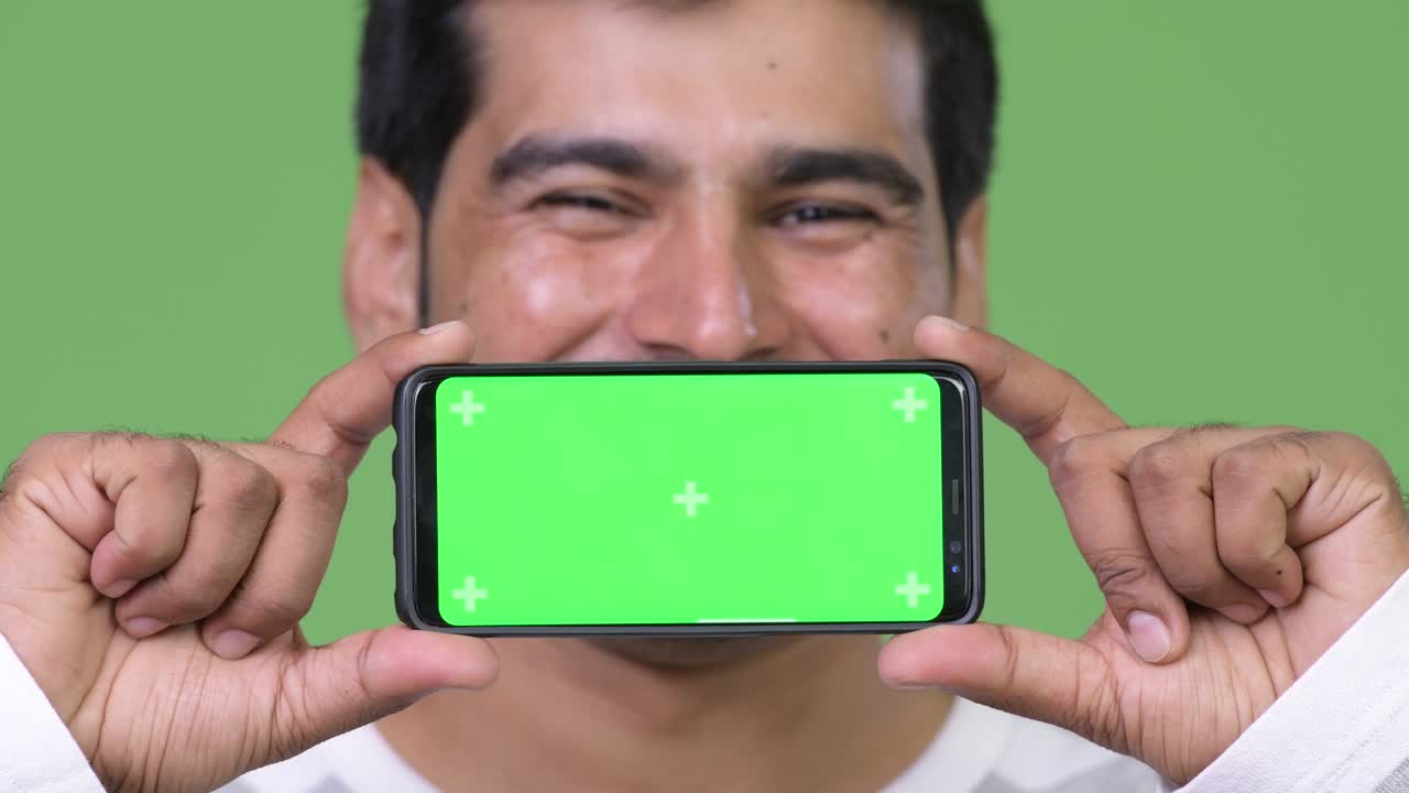 젊은 잘생긴 페르시아인 남자가 전화를 보여줍니다.