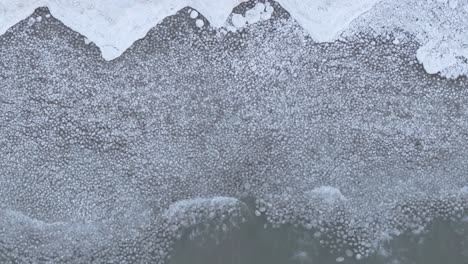 a frozen lake with scattered ice and bubbles trapped under the surface, in the cold embrace of winter, aerial view