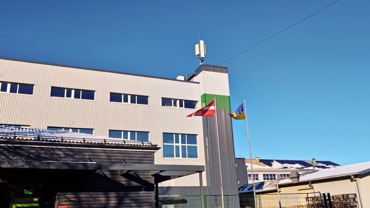 Letlands og Ukraines flag vajer ved en dronefabriksbygning, hvilket symboliserer internationale relationer.