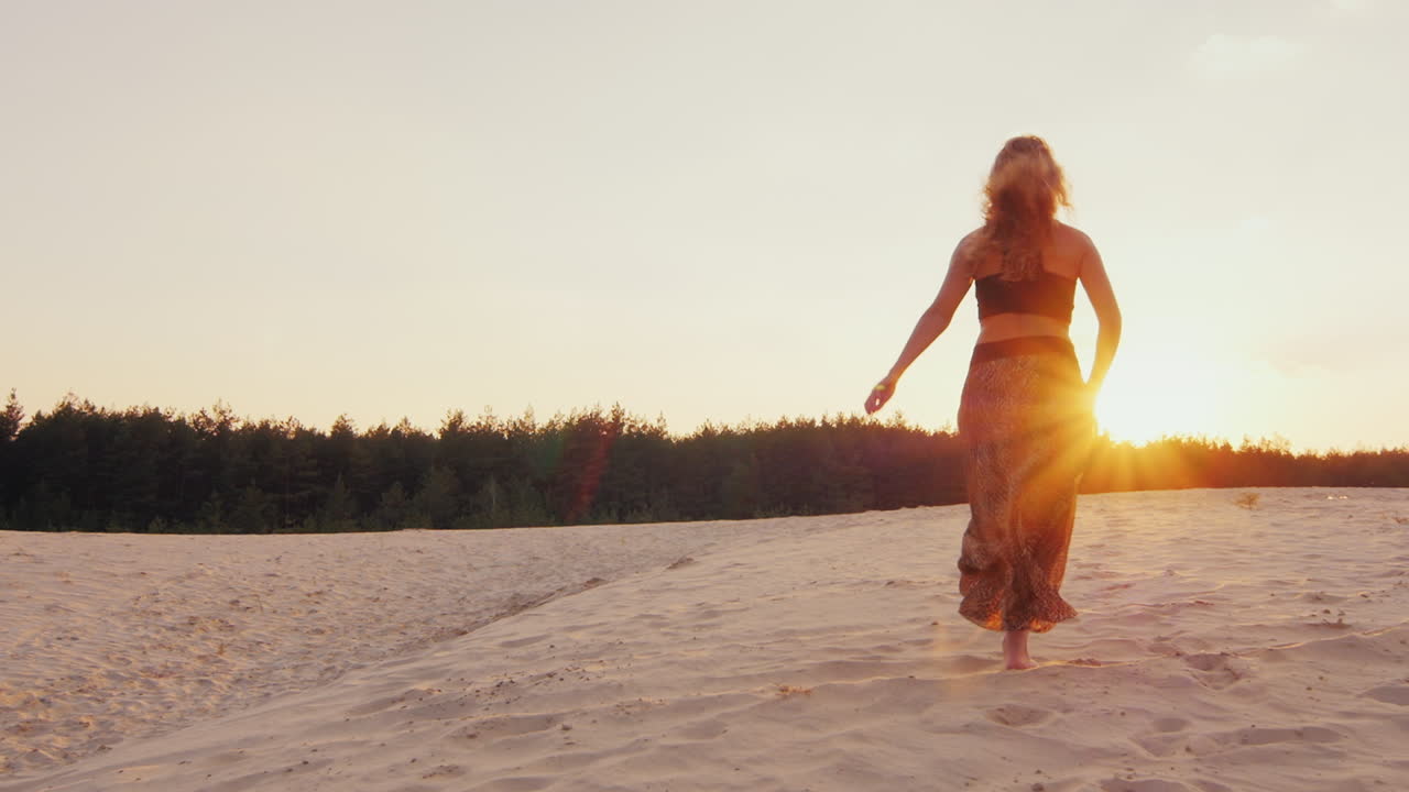 mujer joven con un hermoso vestido ligero corre a lo largo de la playa hacia la puesta de sol estirando los brazos hacia t