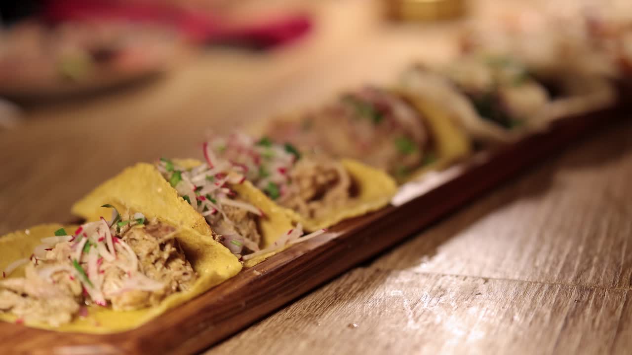 Hands arrange tacos on a wooden platter in a warmly lit restaurant environment, highlighting fresh ingredients and culinary preparation