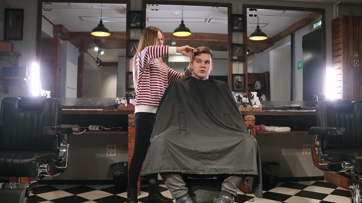 Rear view of man client visiting haidresser and hairstylist in barber shop.