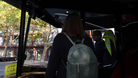 woman with a backpack pays her fare on a london bus with the driver watching attentively