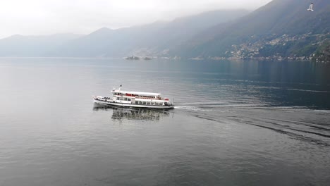 aerial view alongside a boat cruising on lago maggiore near ascona in ticino, switzerland with seagulls flying alongside and a view of the swiss alps on a cloudy day