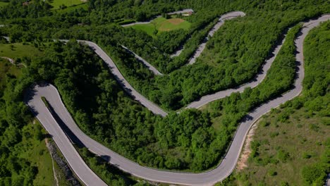 curved asphalt road carved through sloping mountain terrain surrounded by greenery and rock faces. shot in selvino, italy (selvino, italia)