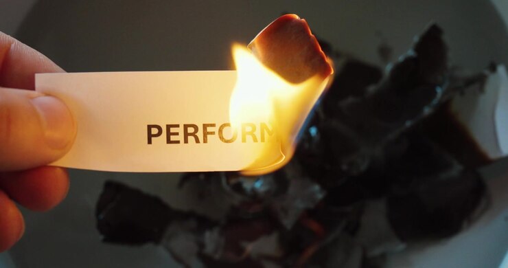 Primo piano di un foglio con la scritta “performance” che brucia, a simboleggiare la perdita, il declino o l'eliminazione della produttività e dell'efficienza.