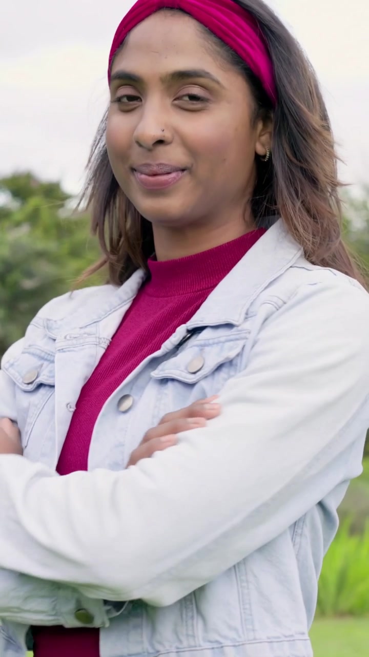 Vídeo vertical: Mulher indiana abrindo os olhos, posando no parque com tiara magenta e ajustando a jaqueta.