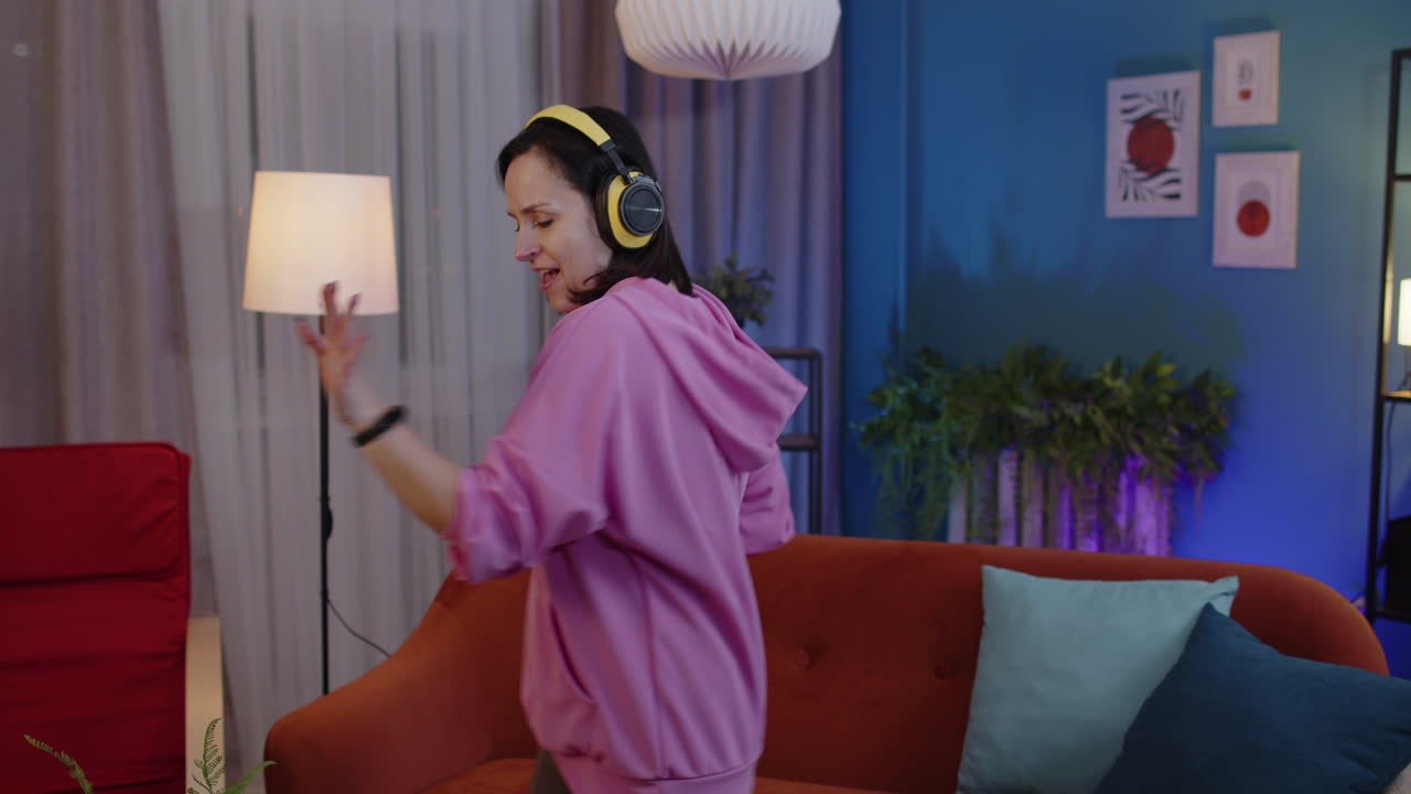 가정에서 혼자 소파에서 음악을 듣는 동안 헤드폰을 들고 춤추고 뛰어다니는 행복한 성인 여성