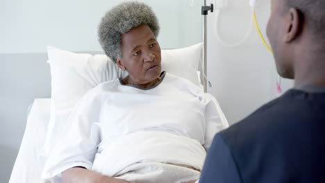 african american male doctor talking with female senior patient in hospital room, slow motion