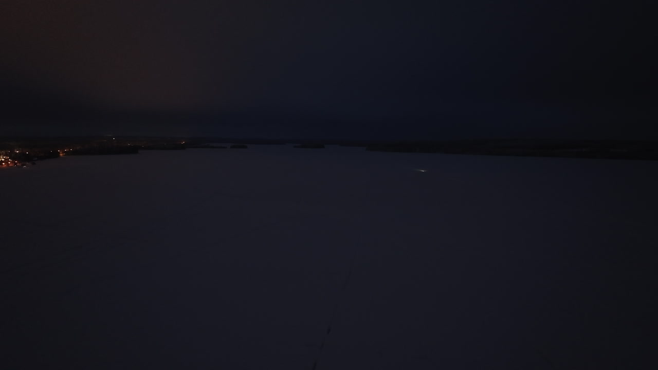 Aerial view of a snowmobile driving on a snowy lake, winter night in Finland