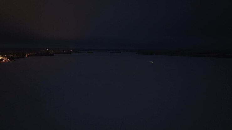 Aerial view of a snowmobile driving on a snowy lake, winter night in Finland