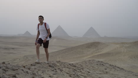 man walks on sand dune with great pyramids of giza in background at sunset