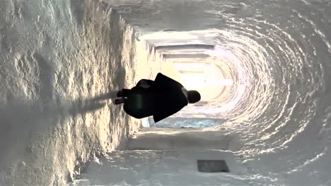 pov walking behind person walking through ice carved ice tunnel at ice hotel towards light