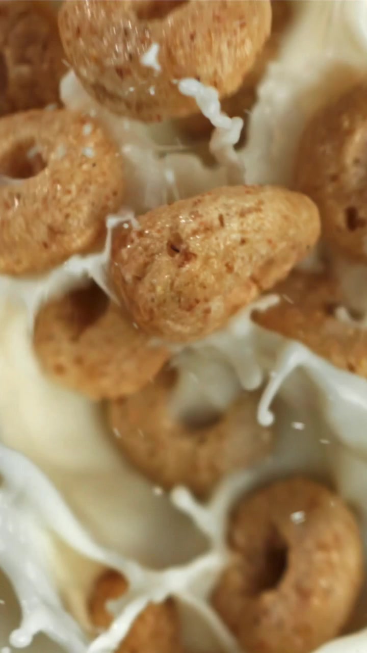 Anelli di cereali per la colazione che cadono e schizzano nel latte al rallentatore.