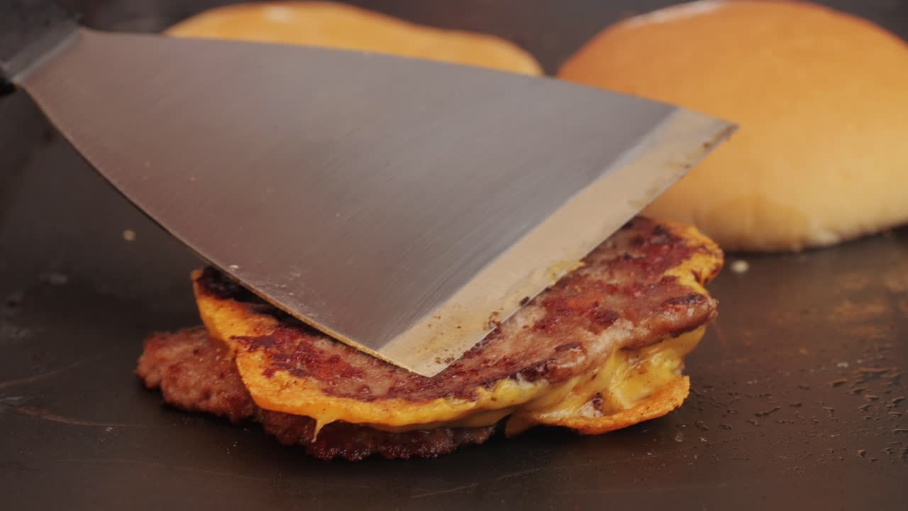 Cooking American fat smash burger with cheese slice on top on grill close-up. Beef or pork cutlet smashing by burger press. The chef in kitchen of the restaurant making cutlets for burgers - smash burger beefsteak. Fast and street food concept.