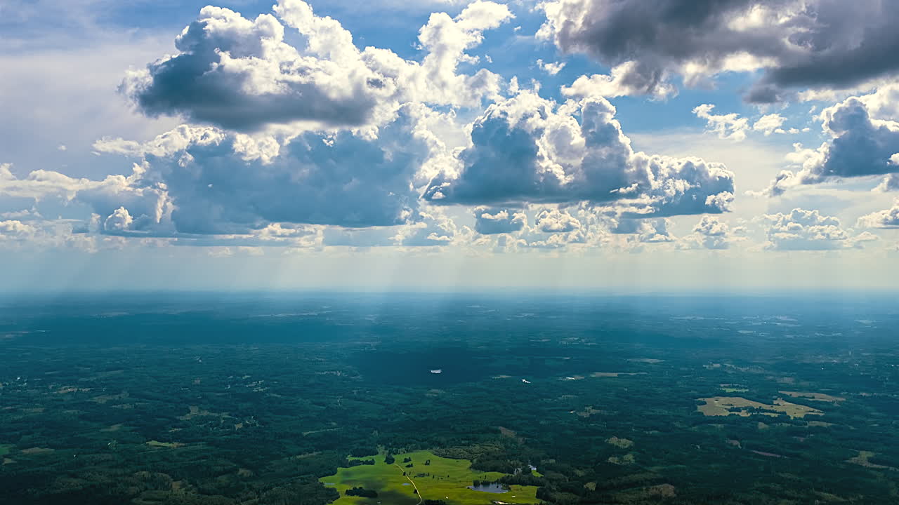 Aerial timelapse showcasing dramatic summer clouds casting shifting light over vast green landscapes and distant horizon