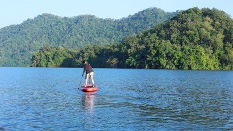 person paddleboarding on calm water with scenic backdrop