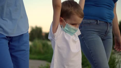una familia con un niño en máscaras médicas caminando cerca del lago 03