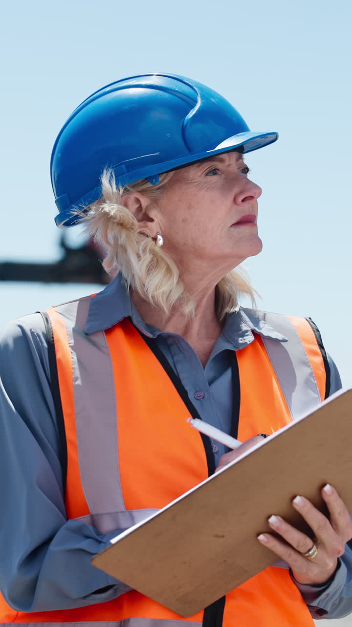 Mature Woman Engineer in Hard Hat and Safety Vest Writing on Clipboard