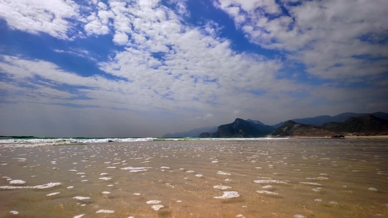Gentles ocean waves on a sandy beach in Oman - low angle view of the sea and landscape