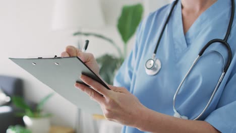 Caucasian-female-doctor-at-home-writing-on-clipboard