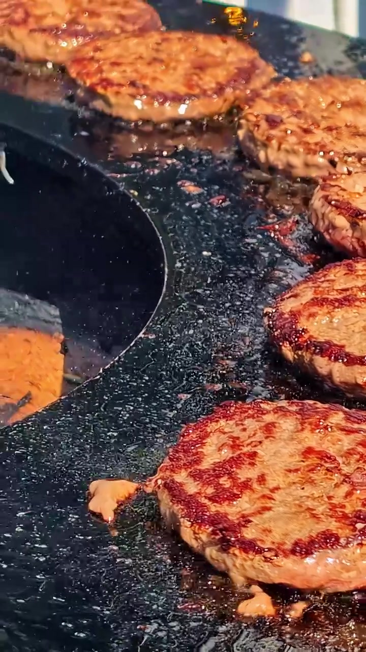 Hamburger di manzo sfrigolano e risplendono su una piastra calda e unta, catturando l'essenza della cucina all'aperto. Ideale per spot pubblicitari alimentari o dimostrazioni culinarie
