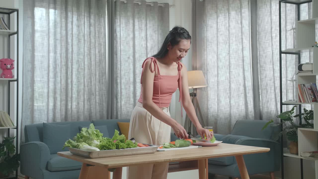 미소 짓는 아시아 여성 이 집 에서 건강 한 음식 을 준비 하는 동안 접시 에 개진 호박 을 넣고 있다