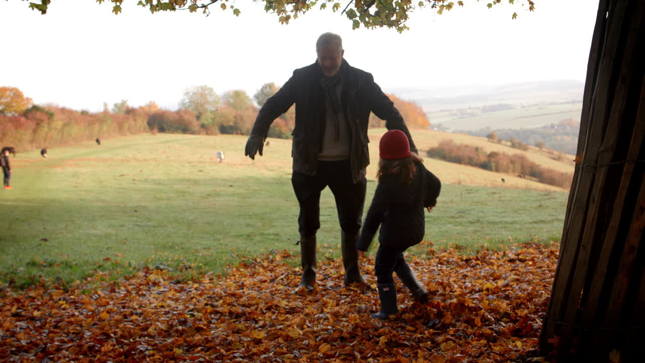 abuelo y nieta pateando hojas en una caminata de otoño